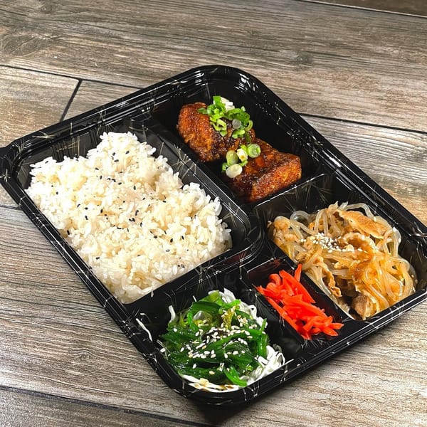 Japanese bento box with rice, teriyaki chicken, seaweed salad, and pickled ginger on a wooden table.
