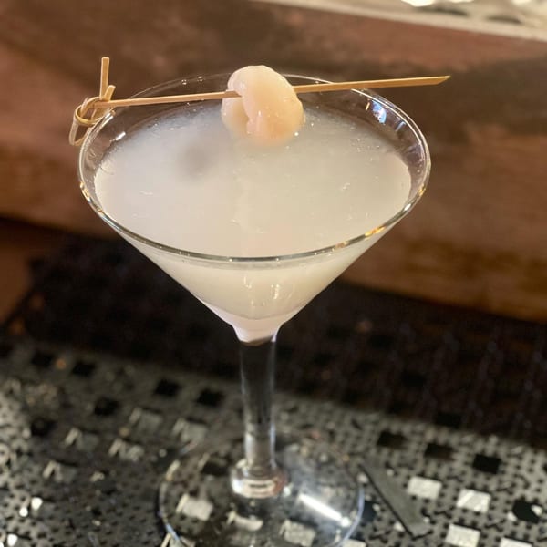Lychee martini in a stemmed glass, garnished with a lychee on a bamboo skewer.