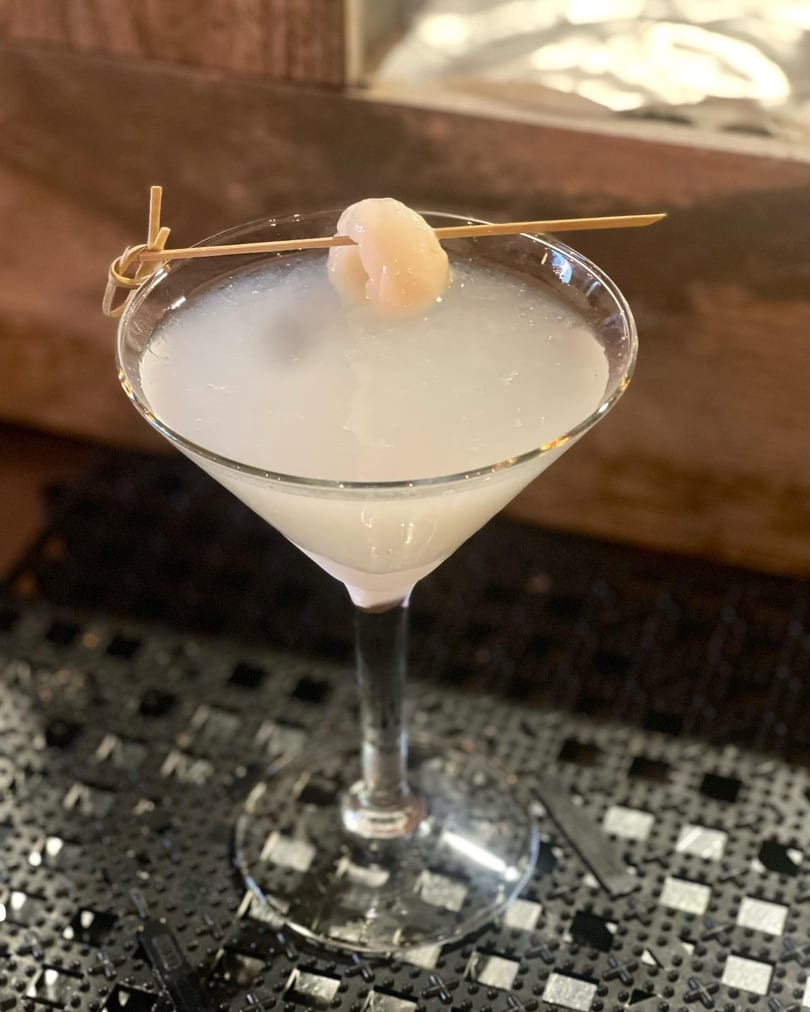 Lychee martini in a stemmed glass, garnished with a lychee on a bamboo skewer.