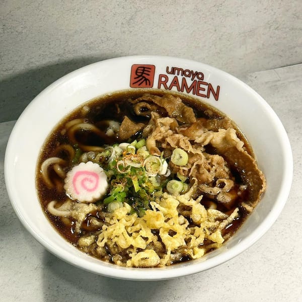 Umaya Ramen bowl with dark broth, noodles, sliced meat, green onions, tempura flakes, and a fish cake.