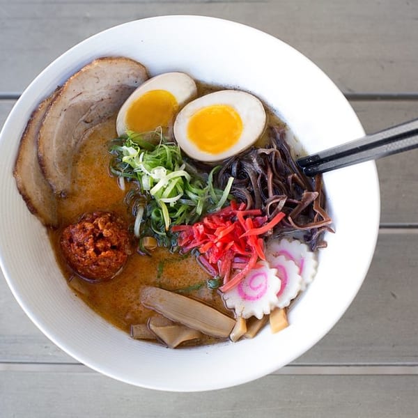 Overhead view of a ramen bowl with pork, soft-boiled eggs, scallions, mushrooms, and red ginger.