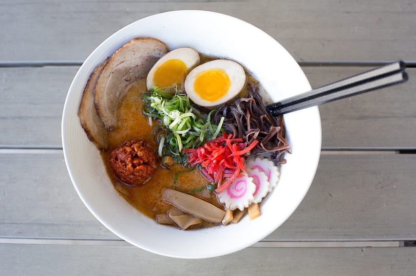 Overhead view of a ramen bowl with pork, soft-boiled eggs, scallions, mushrooms, and red ginger.