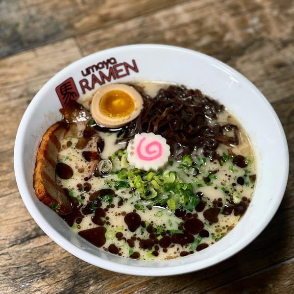 A bowl of Umaya Ramen with pork, egg, mushrooms, green onions, and a pink swirl.