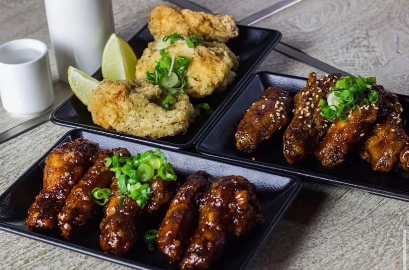 Three plates of chicken wings, two glazed with sauce and one crispy fried with lime.