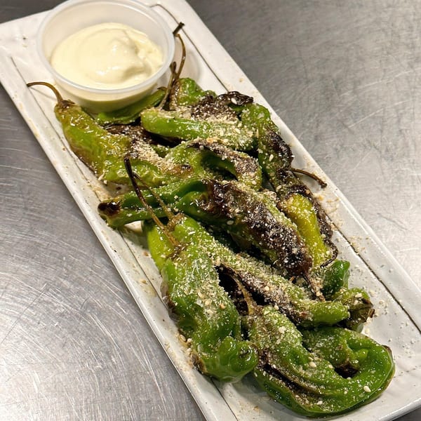 Blistered shishito peppers with sesame seeds and a side of creamy white dipping sauce.