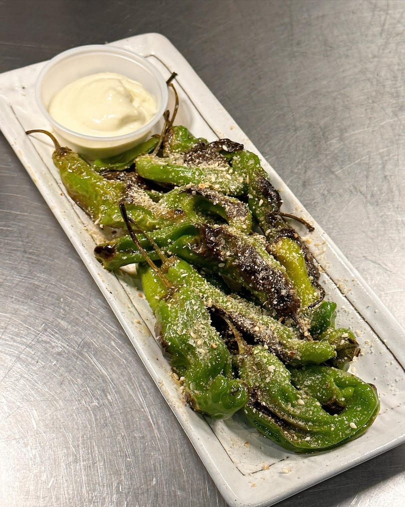 Blistered shishito peppers with sesame seeds and a side of creamy white dipping sauce.