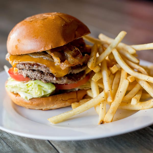 A double cheeseburger with bacon, lettuce, tomato, and fries on a white plate.