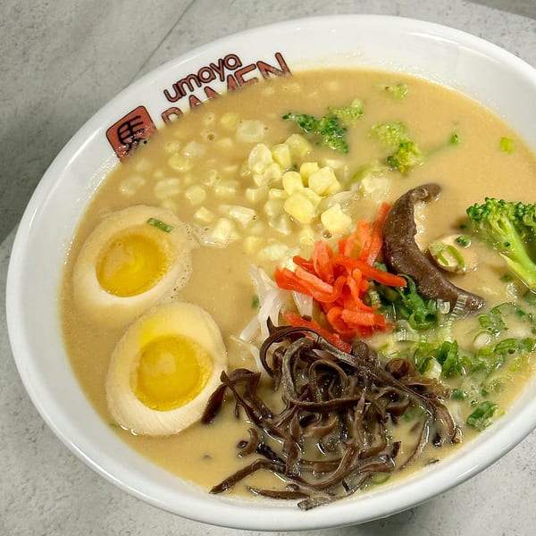 A bowl of Umaya Ramen with broth, corn, broccoli, mushrooms, scallions, and two soft-boiled eggs.