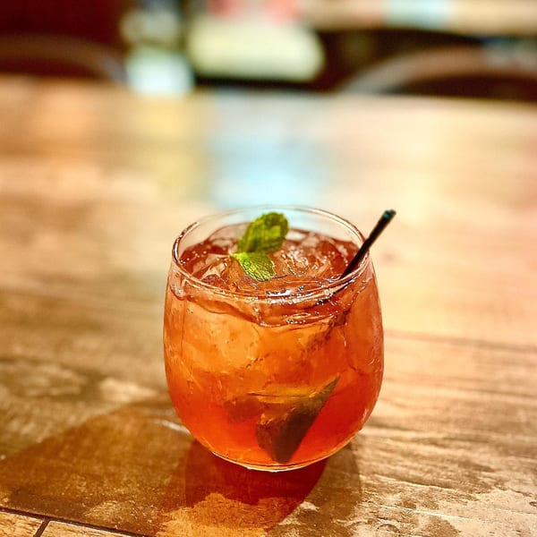 A refreshing iced tea with mint and a straw in a glass on a wooden table.