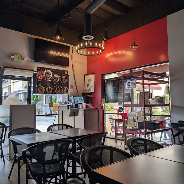 Interior of a modern restaurant with black tables and chairs, red accent wall, and exposed ceiling.