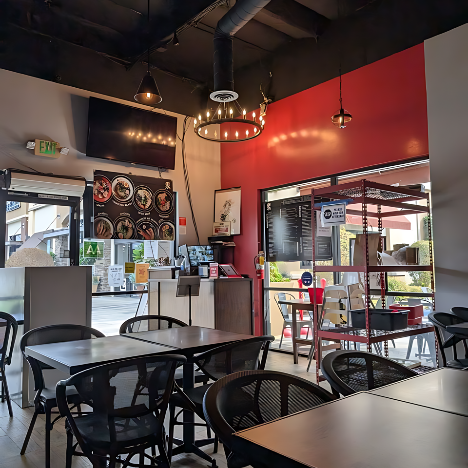 Interior of a modern restaurant with black tables and chairs, red accent wall, and exposed ceiling.