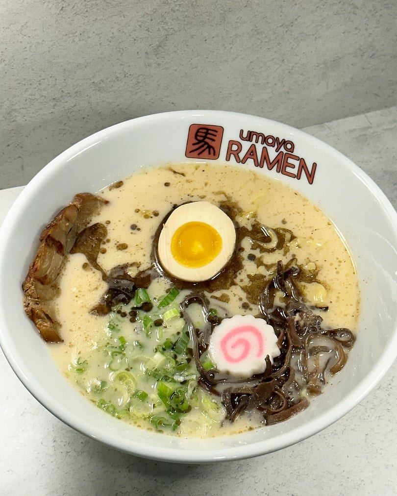 A bowl of Umoya Ramen with pork, egg, green onions, and a pink swirl fish cake.